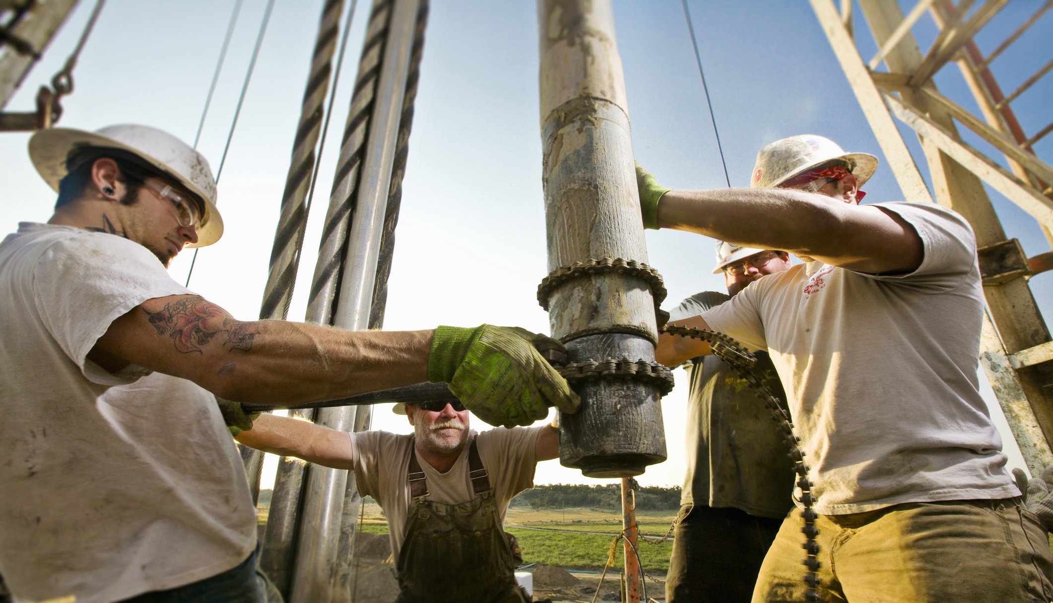 Oil workers using chain to position drill on drilling platform
